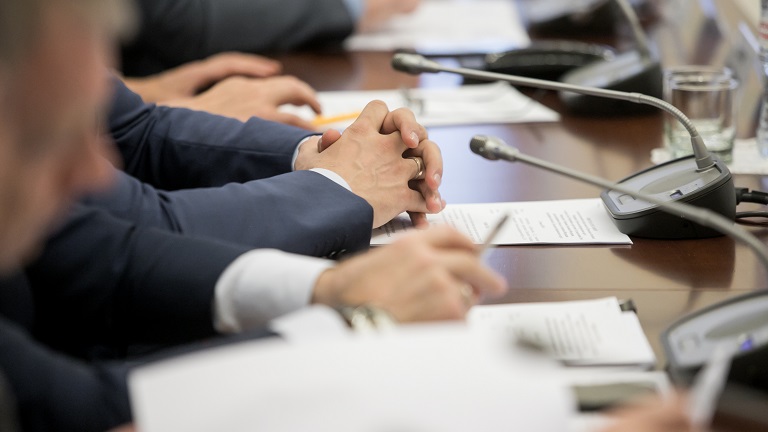 One of politician sitting by table with his hands over document during political summit or conference