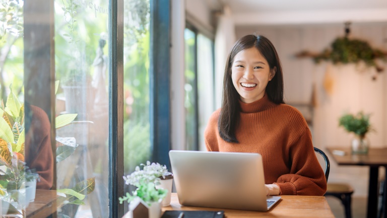 Happy young Asian girl working at a coffee shop with a laptop 